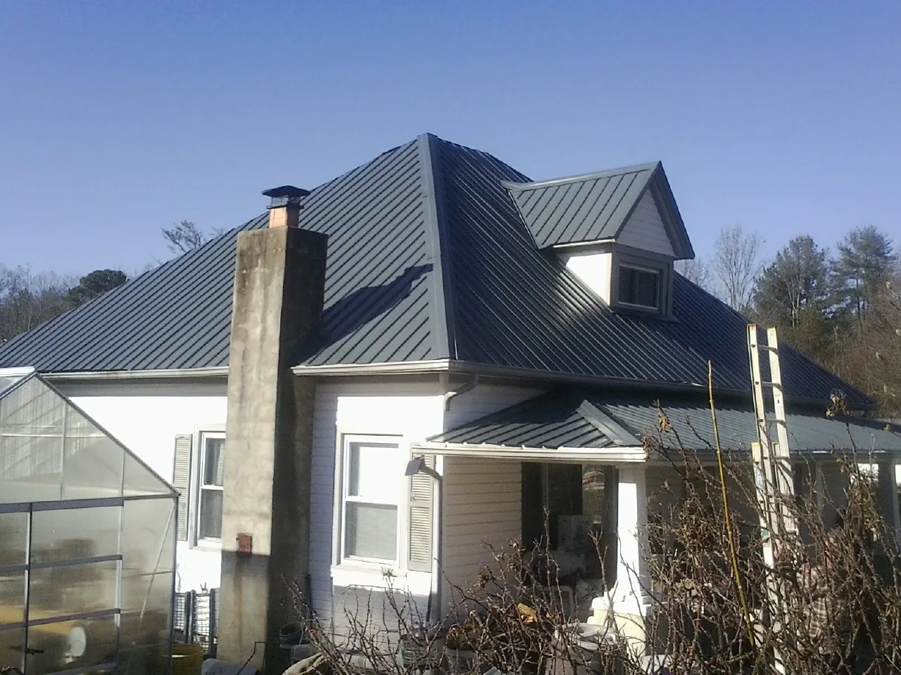 Dark blue standing seam metal roof on a white farmhouse with dormer — Slate & Tile Roof Repair by Roofing Brothers in Bohannon