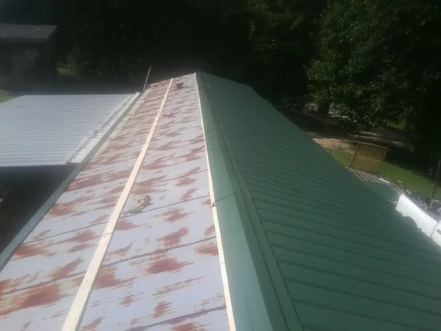 Old rusted panels beside newly installed green metal roofing — Wind Damage Roof Repair by Roofing Brothers in Bohannon