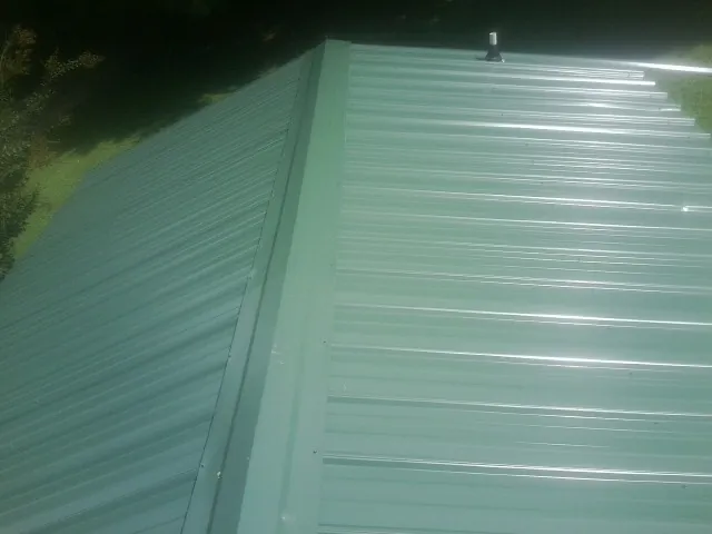 New green metal panels meeting at the ridge of a roof — Flat Roof Repair work by our crew in Bohannon