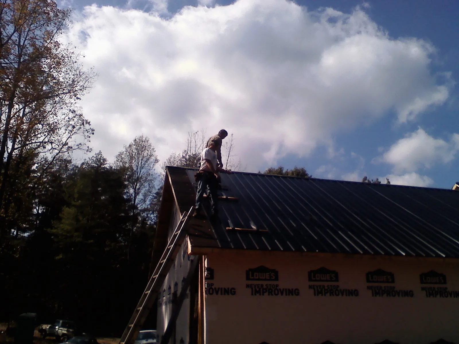 Roofer fastening dark metal panels high against a cloudy sky, from a Roof Inspection job in Bohannon