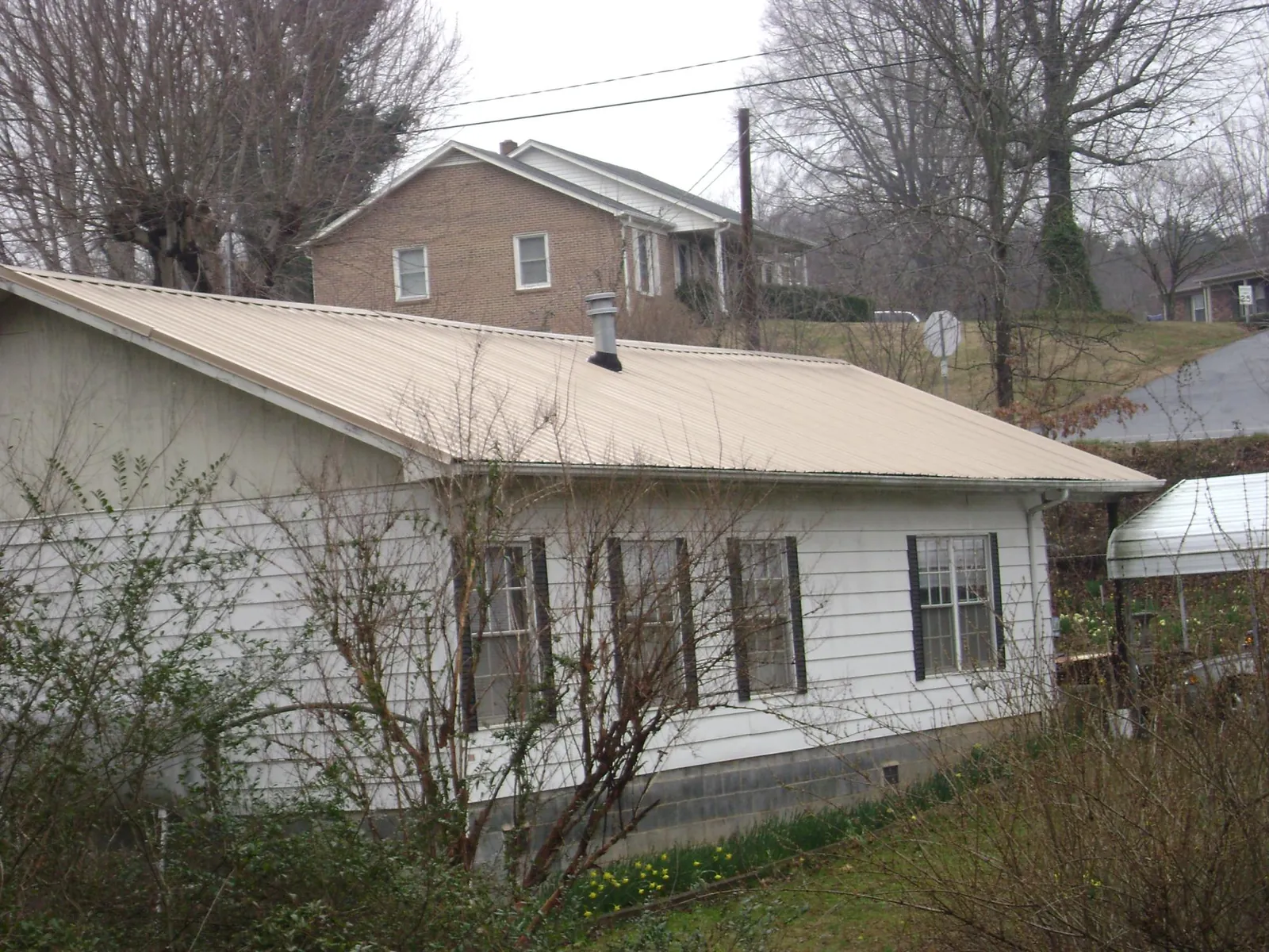 Tan metal roof on a white sided house set into a hillside — Commercial Roofing by Roofing Brothers in Bohannon